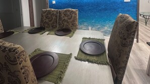 A dining area with a table set for four, a blue wall mural, and patterned chairs. - Oceanfront Comfort Unit#1 (Corpus Christi)