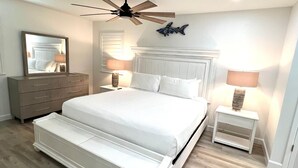 A bedroom with a large bed, a dresser, a ceiling fan, and two bedside lamps. - Oceanfront Comfort Unit#1 (Corpus Christi)