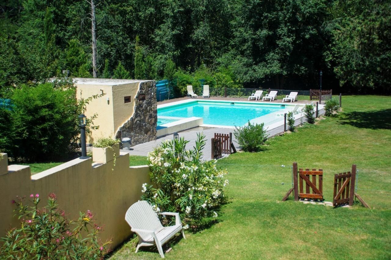 A rectangular swimming pool with a stone wall on one side, surrounded by a wooden fence and several lounge chairs.