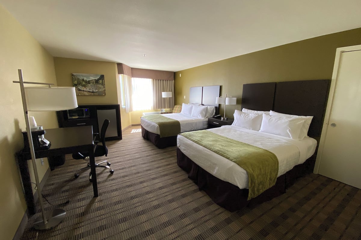 A hotel room with two beds, a desk with a computer, a chair, and a lamp.