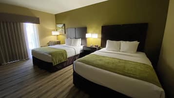 Una habitación de hotel con dos camas, un ventanal grande con cortinas, un cabecero y una mesita de noche con lámpara.