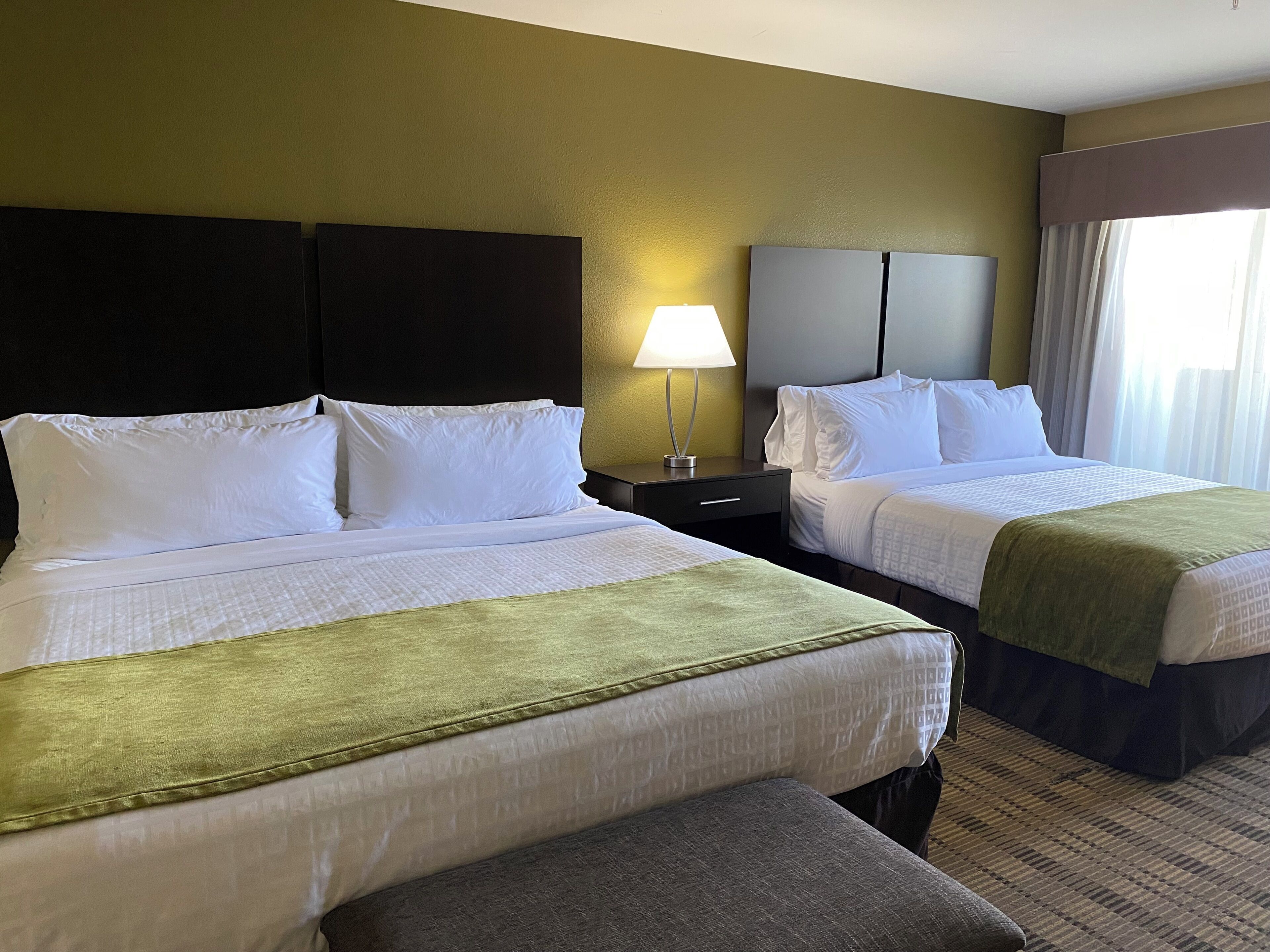 Een hotelkamer met twee bedden, een nachtkastje met een lamp en een raam met gordijnen.