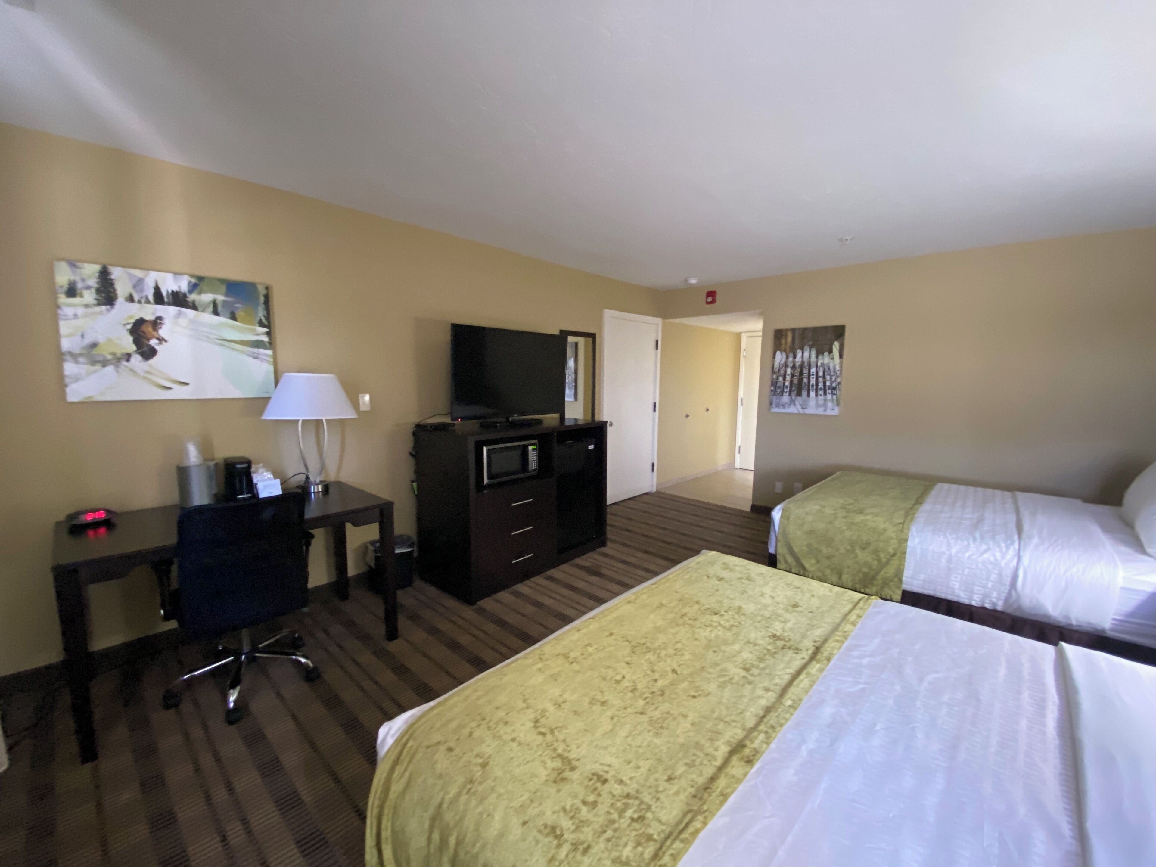 Quarto de hotel com duas camas, uma escrivaninha com computador, televisão e micro-ondas.