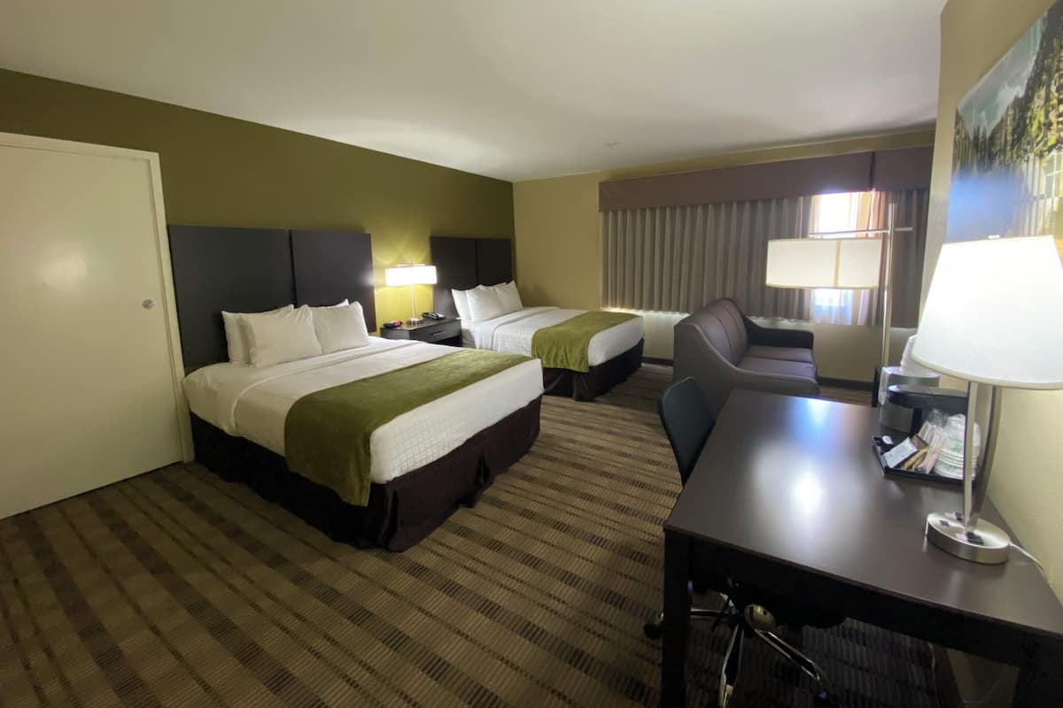 A hotel room with two beds, a desk, a chair, and a lamp.