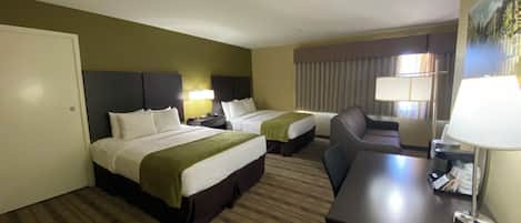 A hotel room with two beds, a desk, a chair, and a lamp.