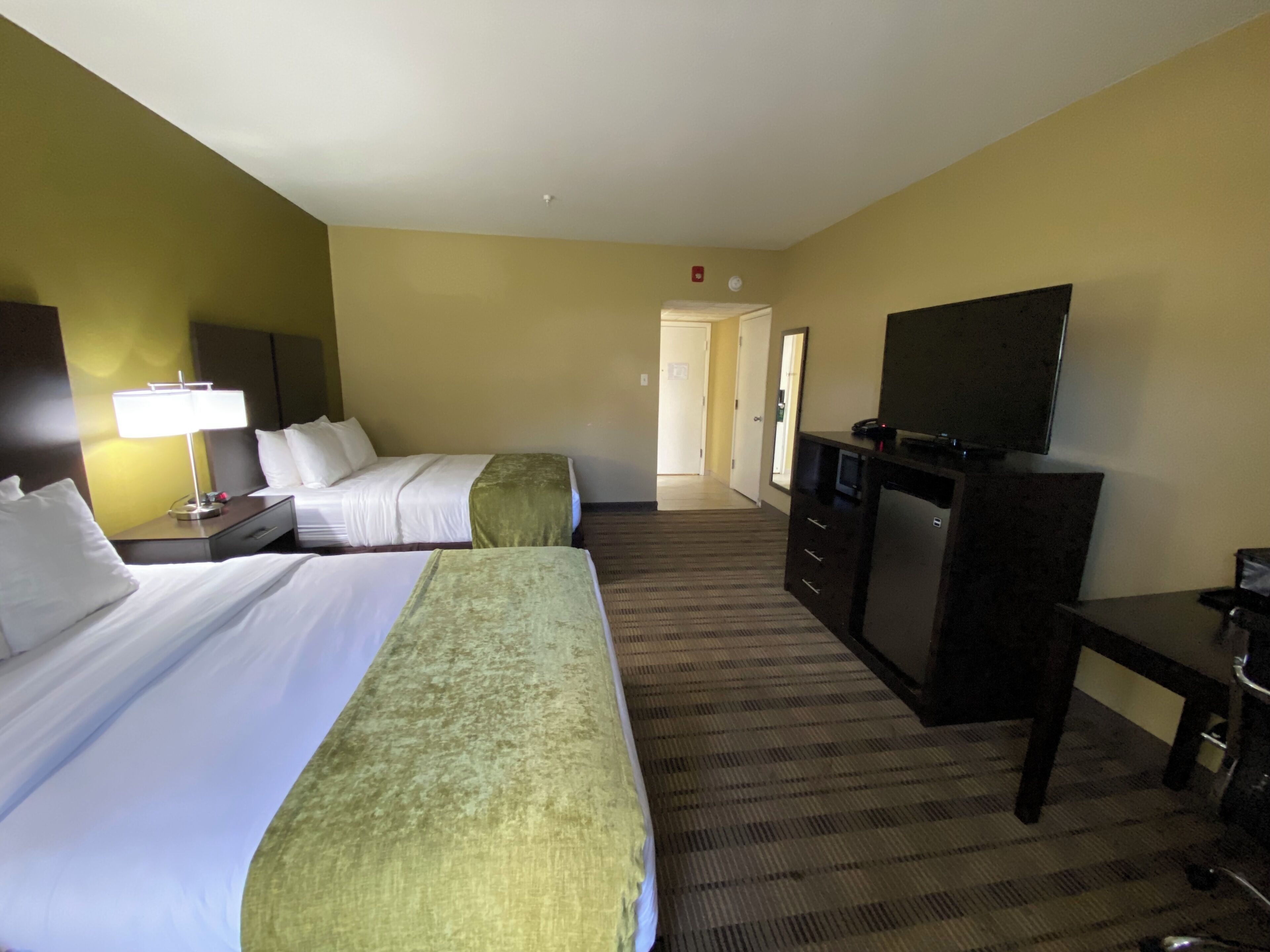 A hotel room with two beds, a desk, a television, and a carpeted floor.