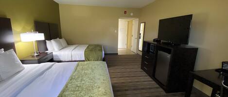 A hotel room with two beds, a desk, a television, and a carpeted floor.