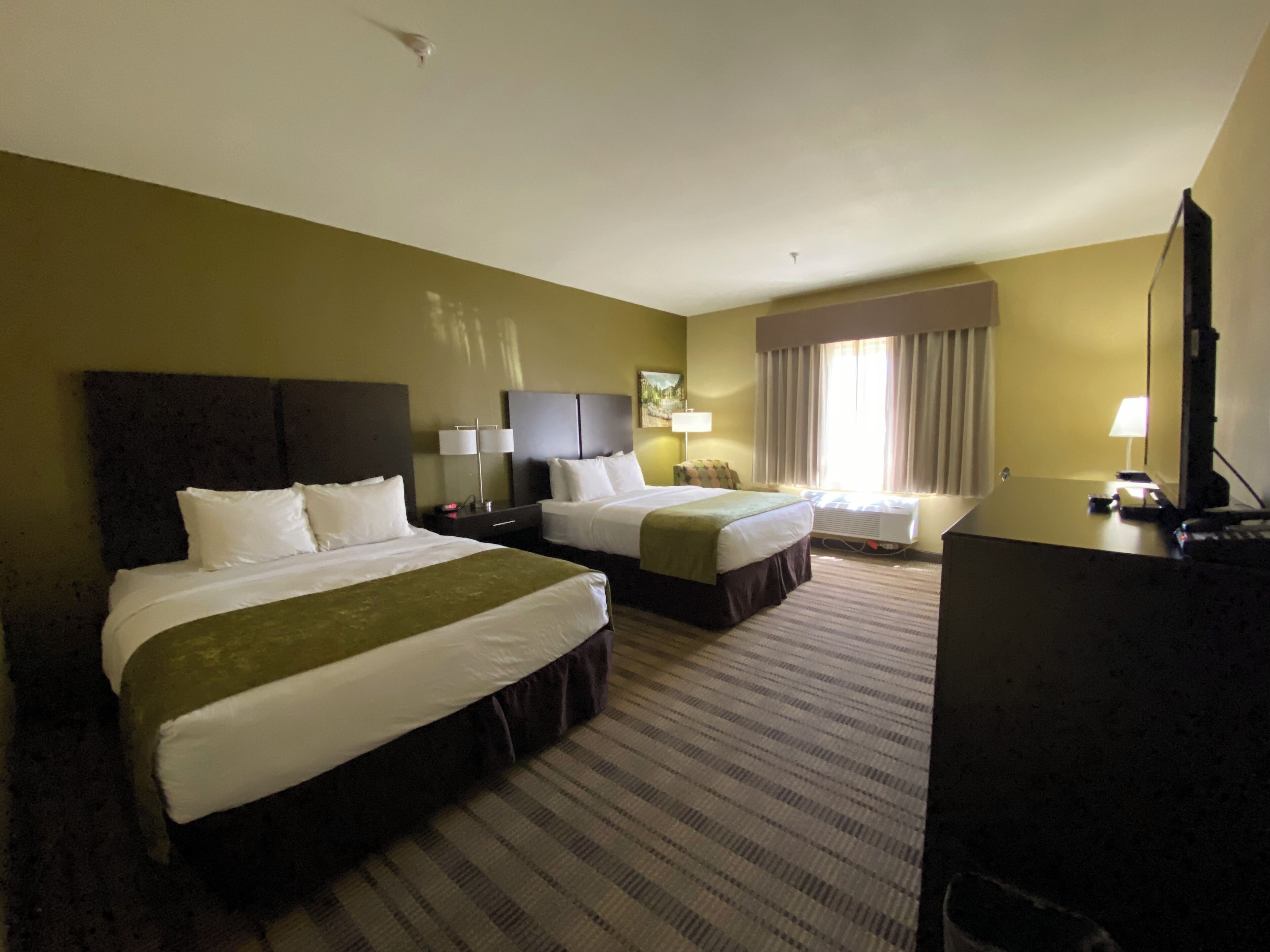Une chambre d’hôtel avec deux lits, un bureau, une chaise, une télévision et une fenêtre avec des rideaux.