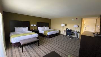 A hotel room with two beds, a desk, a chair, a small table, and a couch.