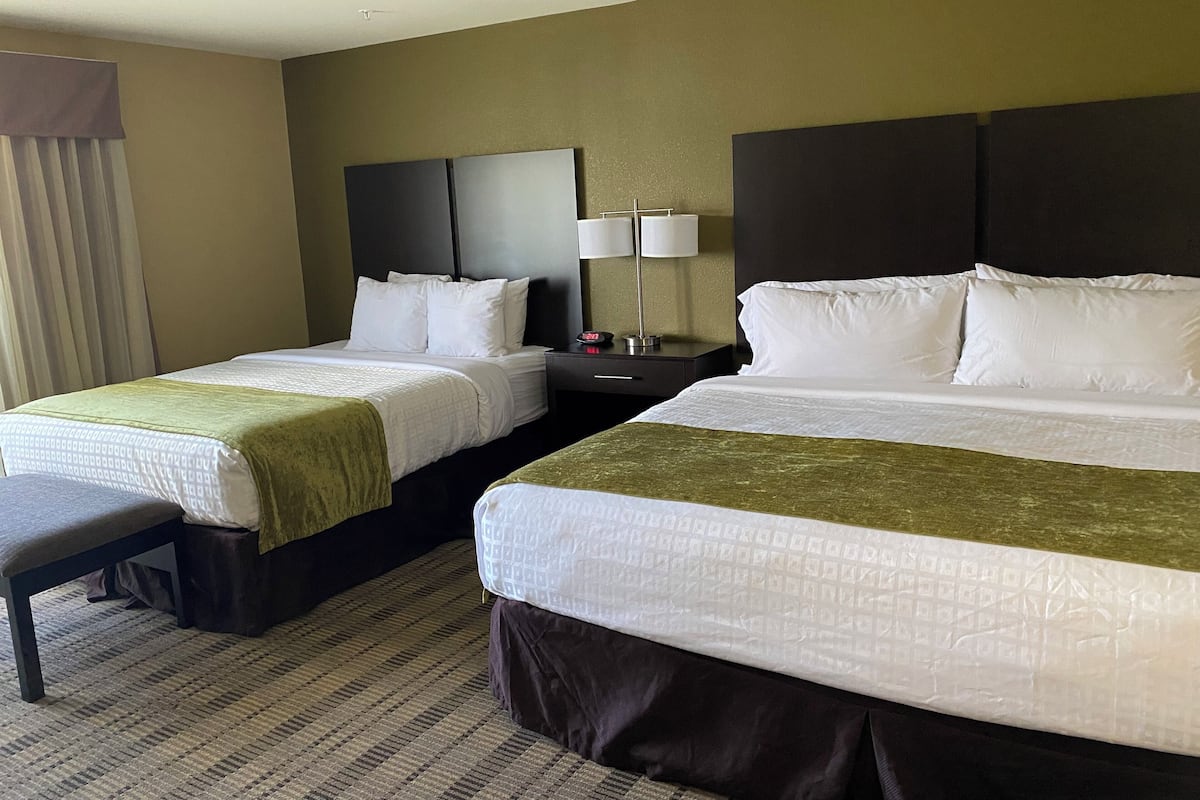 A hotel room with two beds, a nightstand with a lamp, and a bench.
