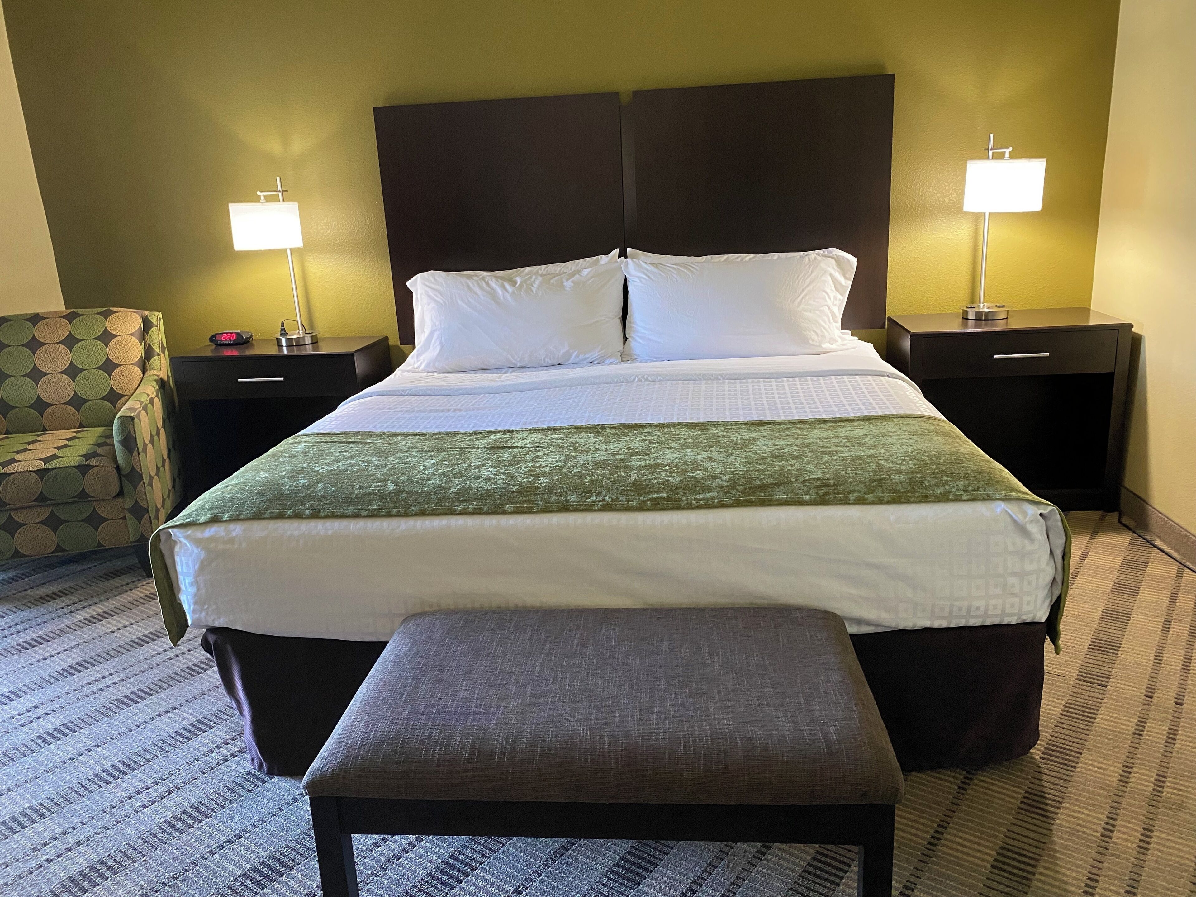 Ein Hotelzimmer mit einem großen Bett, zwei Nachttischen inklusive Lampen, einem Sessel und einer Bank.