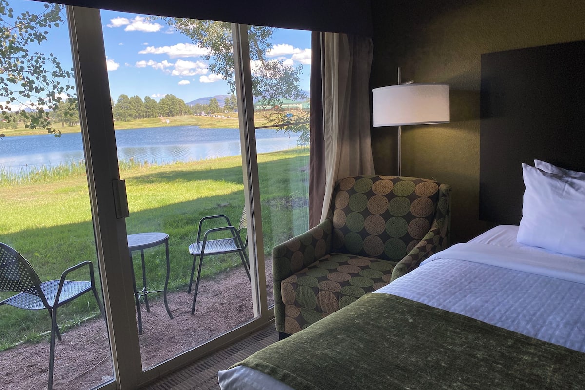 A hotel room with a bed, a chair, a table, and a view of a lake.