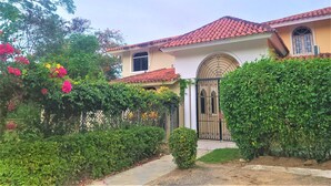 A house with a tiled roof, a gated entrance, and lush greenery. - Linkzup Playa Laguna Villa (Sosúa)