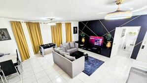 A modern living room with a sofa, coffee table, and foosball table. There is a TV on a black stand and a ceiling fan. - Linkzup Playa Laguna Villa (Sosúa)