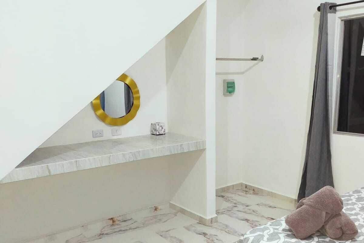 A bedroom with a bed, a bedside table, a mirror, and a window with curtains.