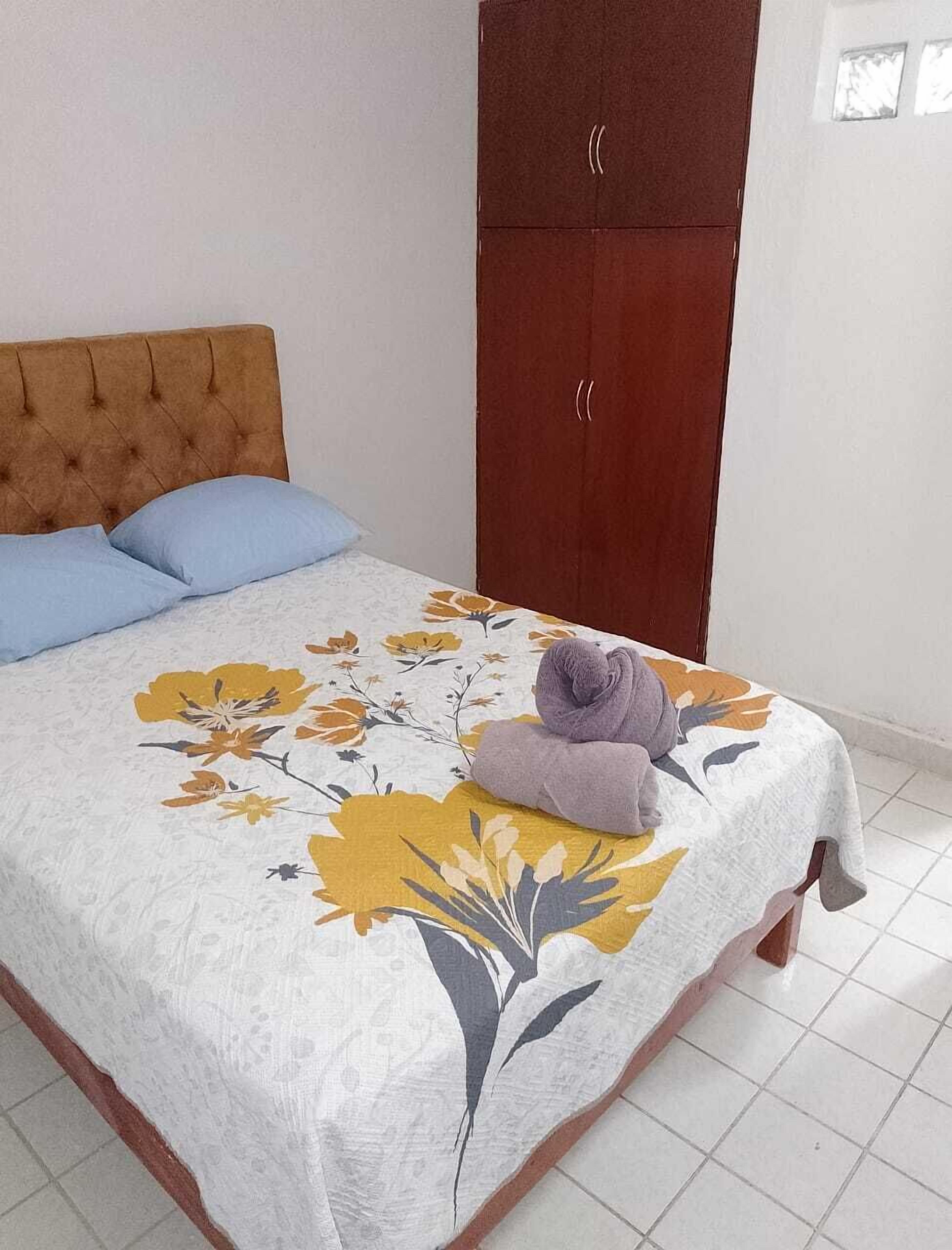 A bedroom with a bed, two pillows, a floral bedspread, and a wooden wardrobe.
