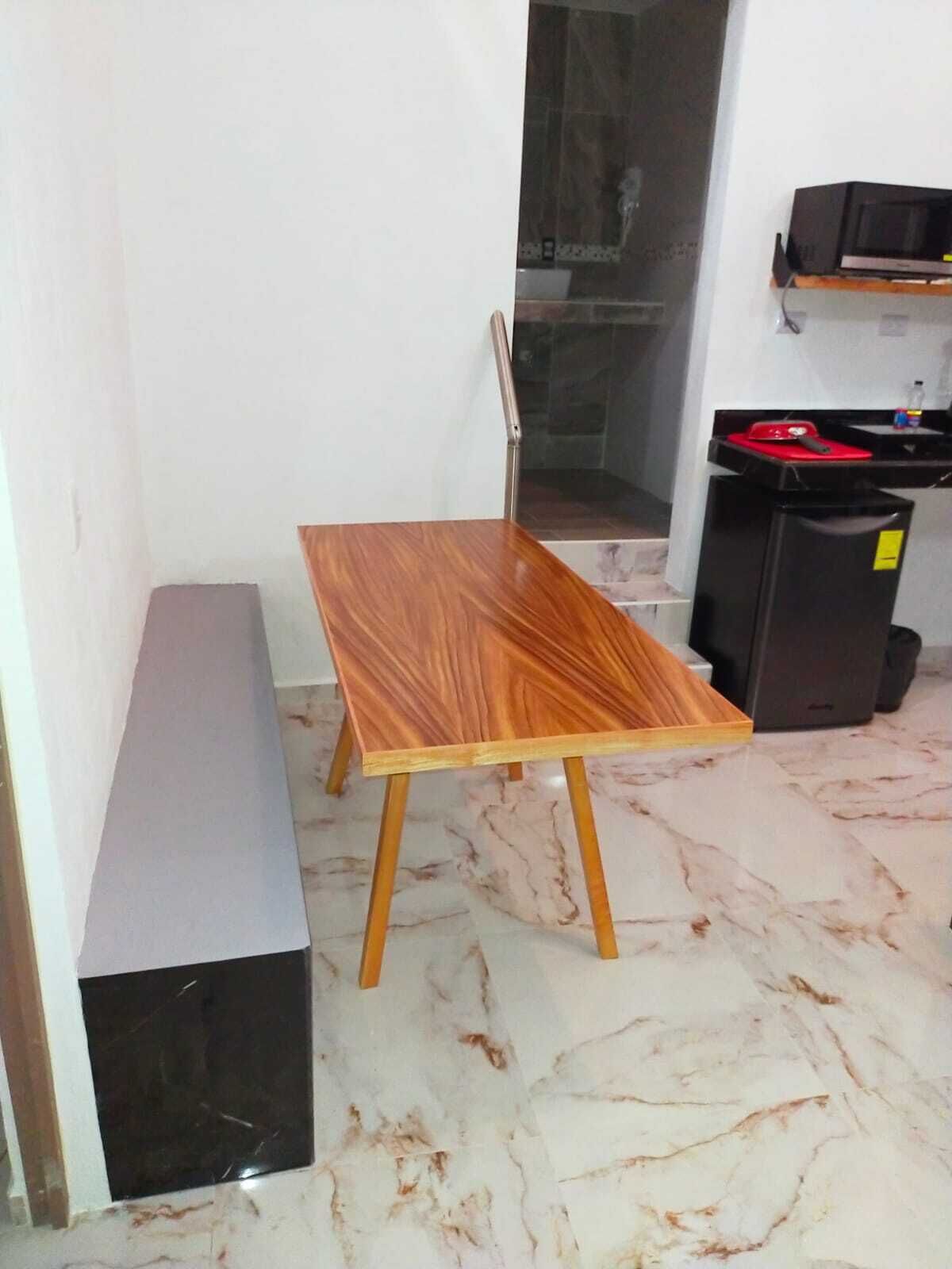 A small room with a wooden table, a bench, and a black trash bin.