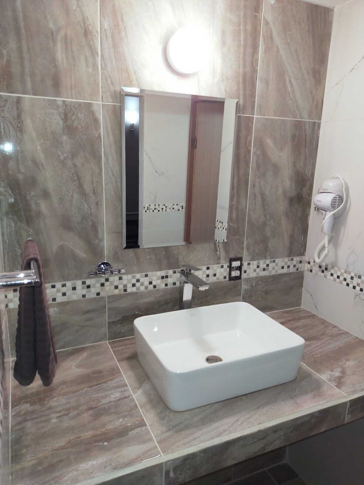 Ein Badezimmer mit einem weißen Waschbecken, einem Handtuchhalter, einem Spiegel und einem an der Wand montierten Föhn.