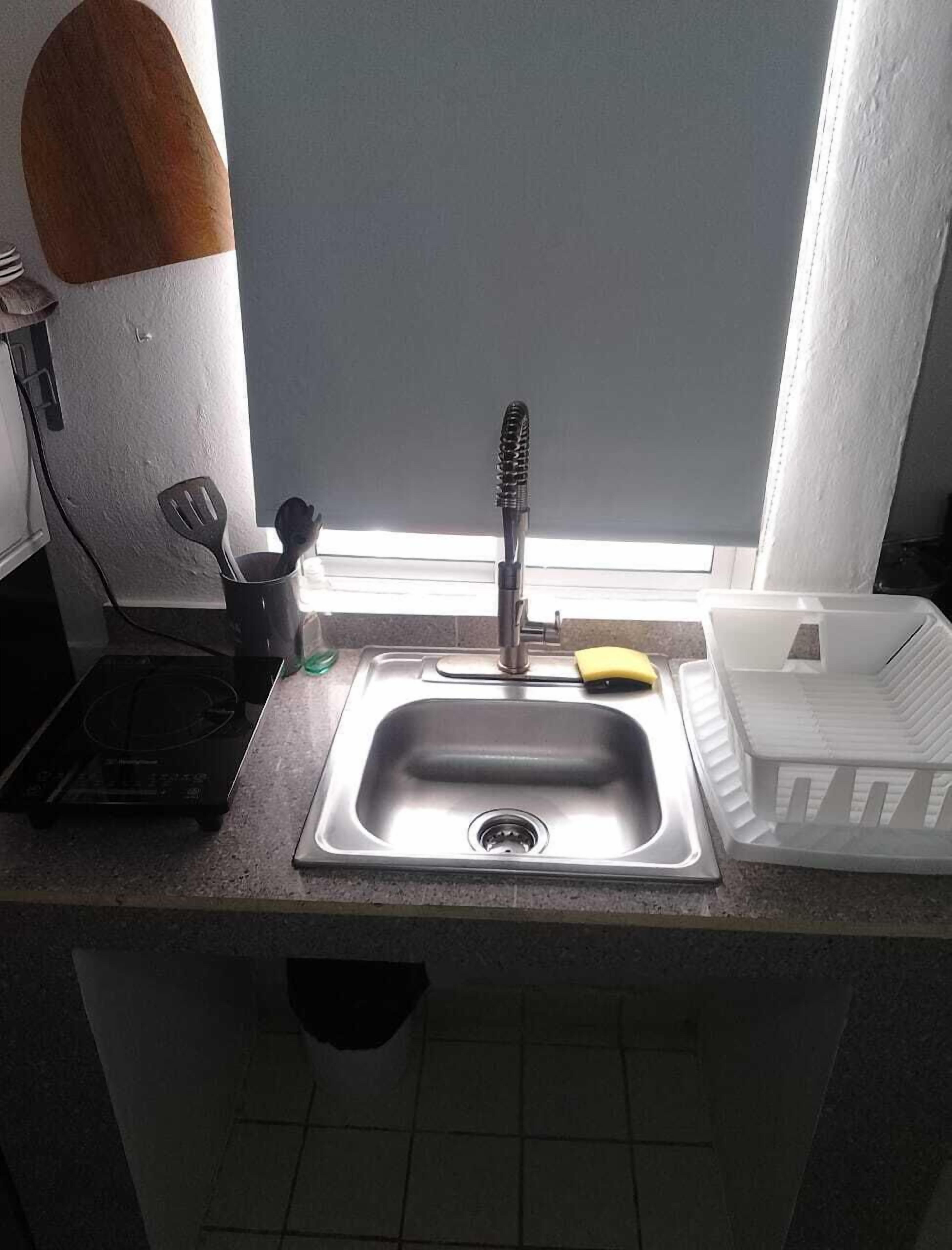 A kitchen with a stainless steel sink, a window, a spatula, and a dish rack.