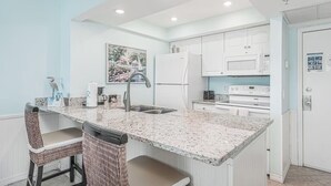 Una cocina moderna con armarios blancos, encimera de granito y pileta integrada. Hay dos sillas de mimbre y una pequeña isla con pileta.