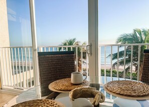 Un balcon agrémenté de meubles en osier, une tasse blanche et une vue sur la plage et les palmiers.