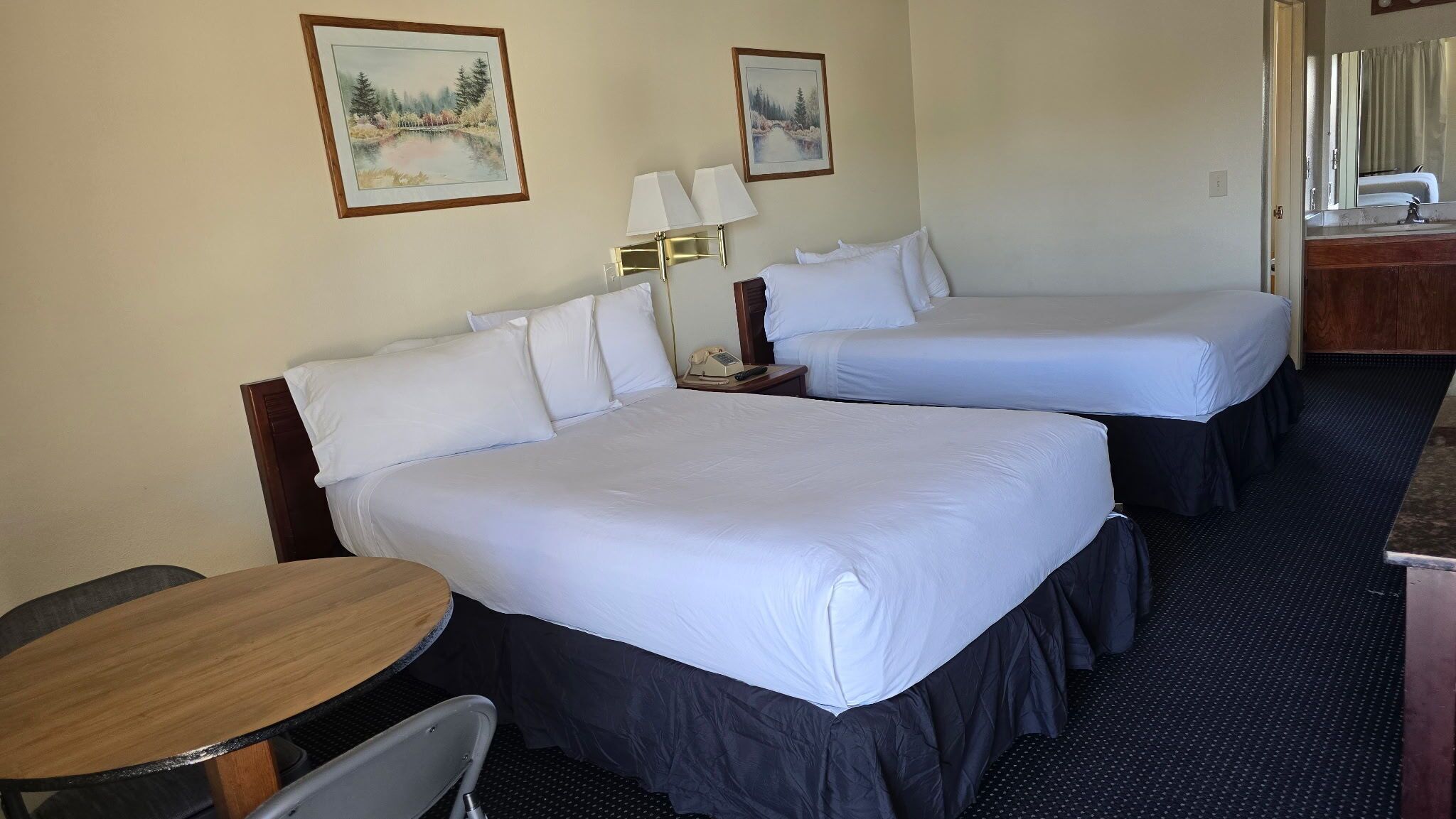 Une chambre d’hôtel avec deux lits, un bureau, une chaise, un téléphone et deux tableaux accrochés au mur.