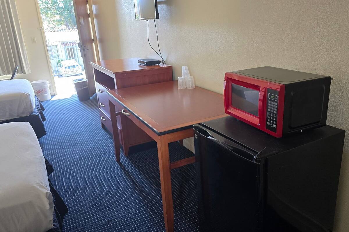 Une chambre d’hôtel avec un lit simple, un bureau en bois, un réfrigérateur noir et un micro-ondes rouge.