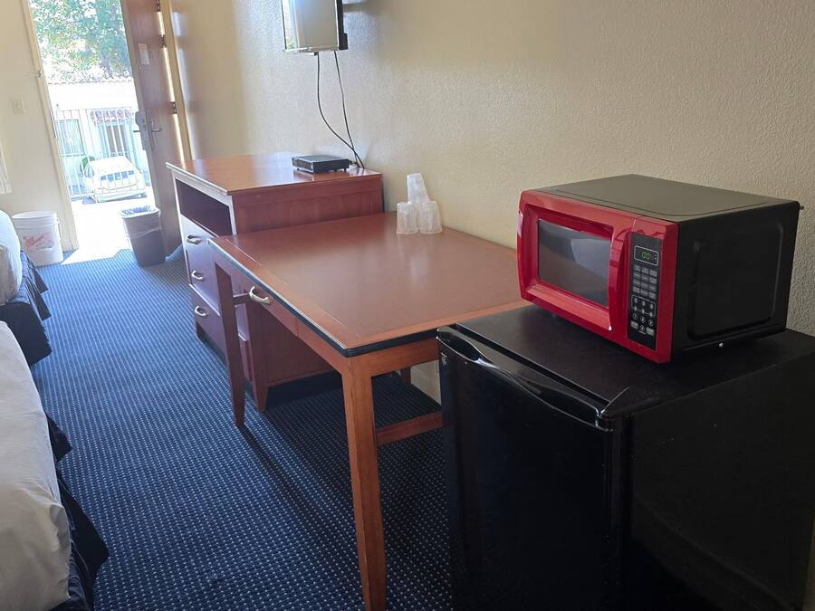 A hotel room with a single bed, a wooden desk, a black refrigerator, and a red microwave.