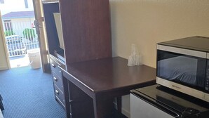 A compact hotel room with a dark wooden desk, a small refrigerator, a microwave, and a bed with white bedding. - Terrace Inn and Suites (Richmond)