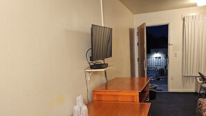 A hotel room with a wooden table, a TV on a stand, a microwave, and a bed with a patterned bedspread. - Terrace Inn and Suites (Richmond)