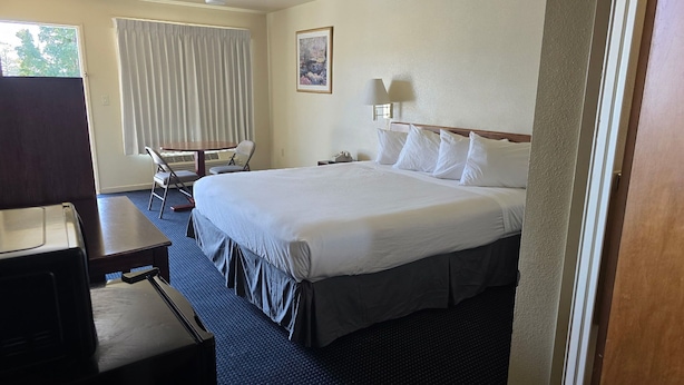 A hotel room with a large bed, a desk, a chair, a window with curtains, and a painting on the wall. - Terrace Inn and Suites (Richmond)