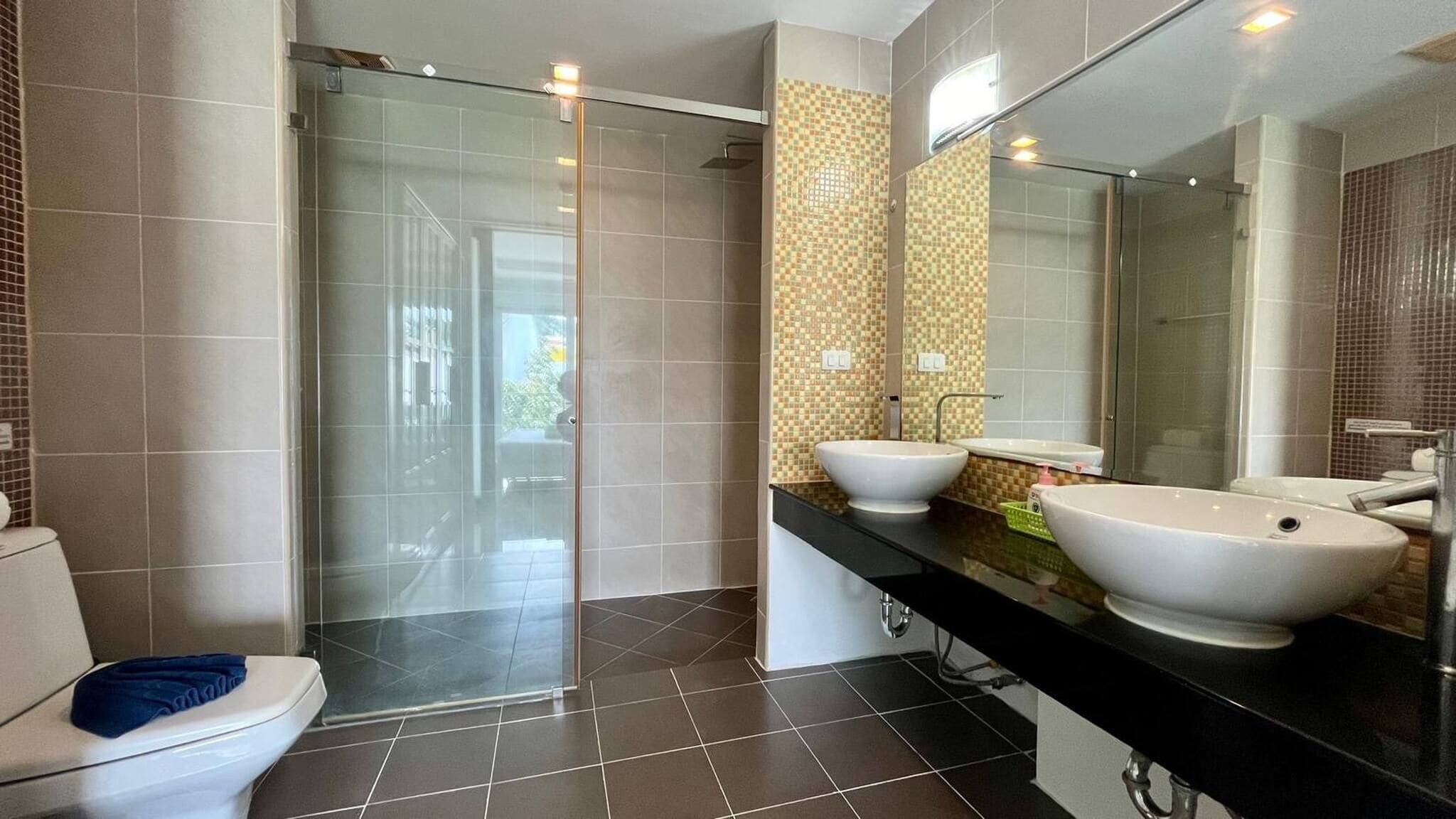 Un baño moderno con ducha de vidrio, dos lavamanos y un inodoro.