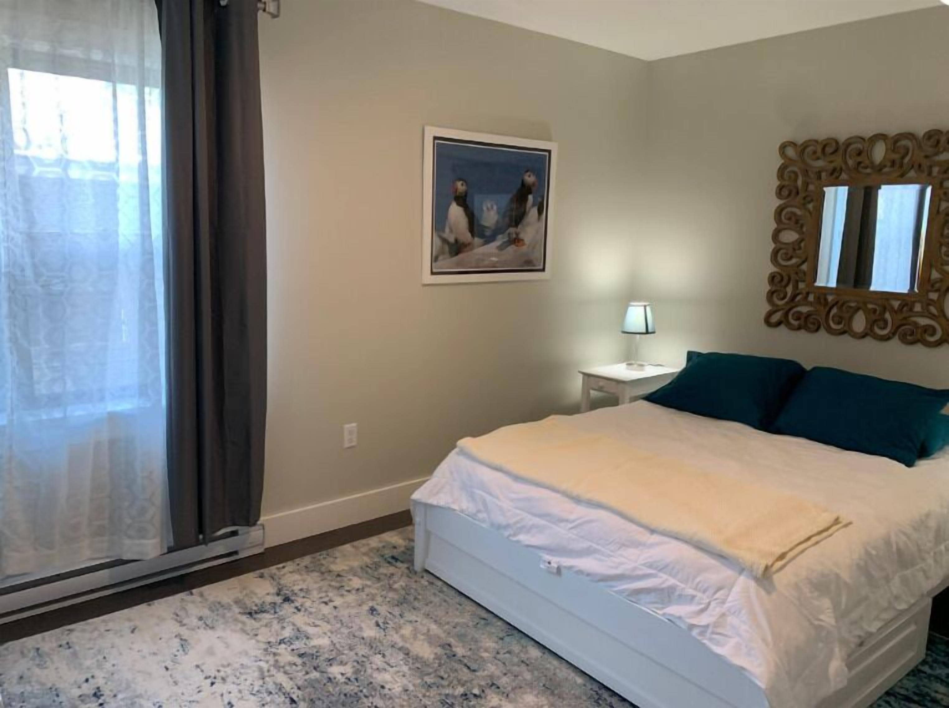 A bedroom with a bed, a nightstand, a lamp, a painting, and a decorative mirror.
