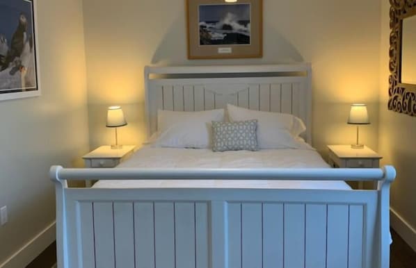 A bed with a white headboard, two bedside tables with lamps, and a framed picture above the bed.