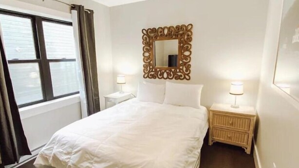 Una camera d'hotel con un letto grande, una ventola a soffitto, una finestra con tende, uno specchio decorativo e lampade ai comodini.