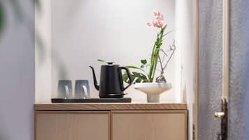 Un mueble de madera con un corte circular, una tetera negra, dos vasos y una maceta con flores rosas.