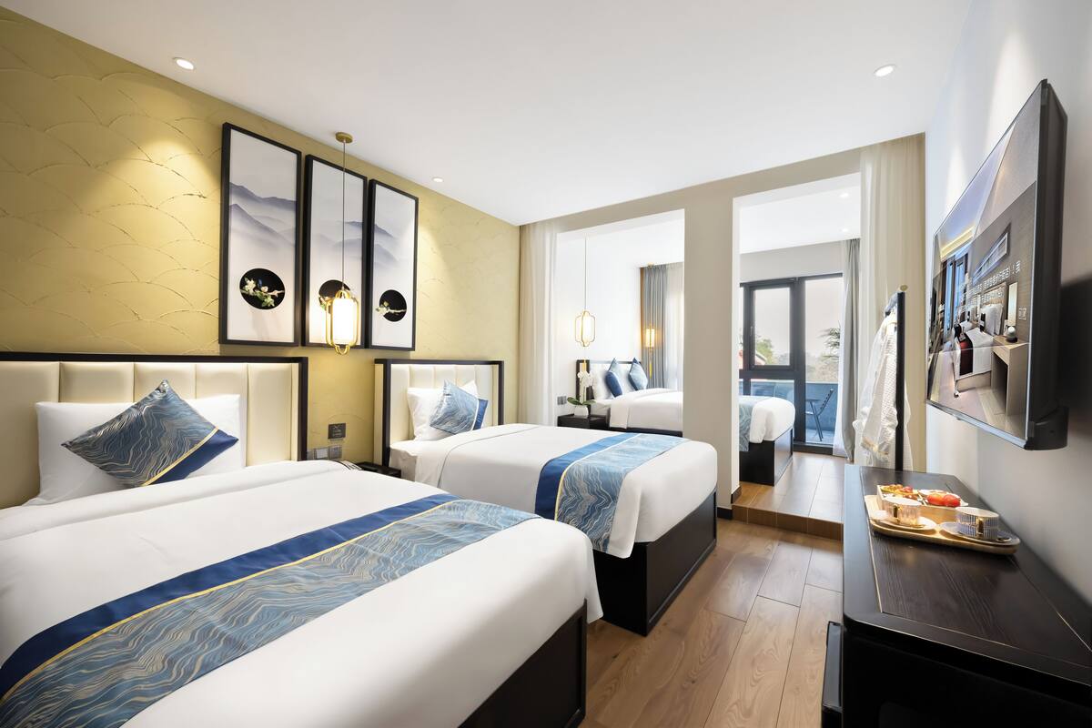Une chambre d’hôtel avec deux lits, une télévision, un bureau avec un plateau de nourriture et une grande fenêtre.