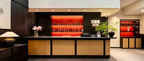 A hotel reception area with a counter, a wall-mounted liquor display, and a potted plant.