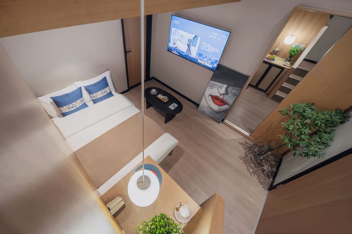 Une chambre d’hôtel moderne équipée d’un lit, d’un petit coin salon, d’un téléviseur fixé au mur et d’un escalier menant à un autre niveau.