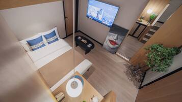 Een moderne hotelkamer met een bed, een klein zithoekje, een aan de muur bevestigde televisie en een trap naar een ander niveau.