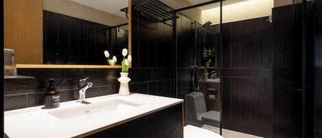 A modern bathroom with a white sink, black tiles, a glass shower enclosure, and a toilet.