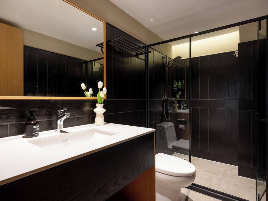 A modern bathroom with a white sink, black tiles, a glass shower enclosure, and a toilet.