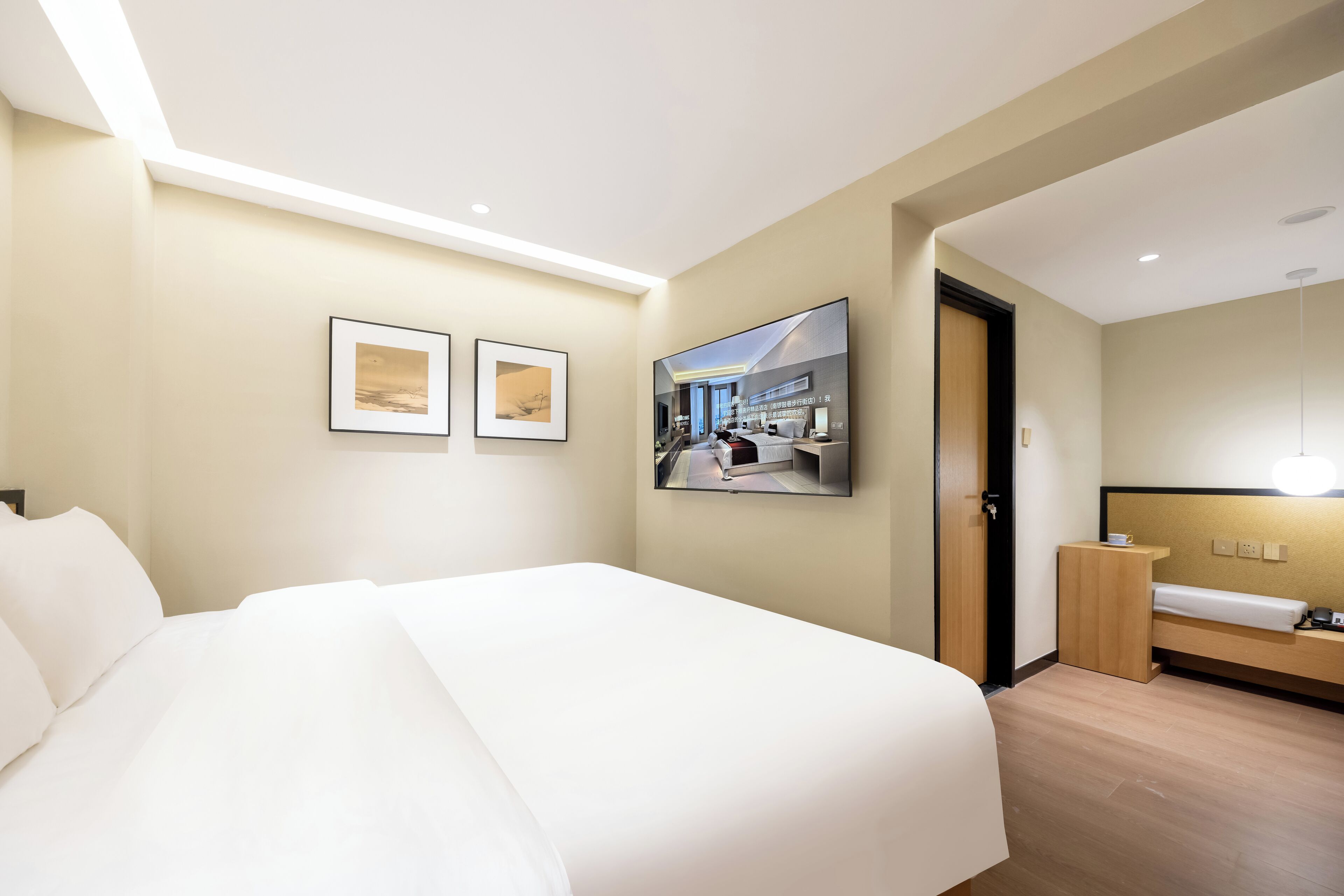 A hotel room with a large bed, a flat-screen TV mounted on the wall, and a small bedside table.