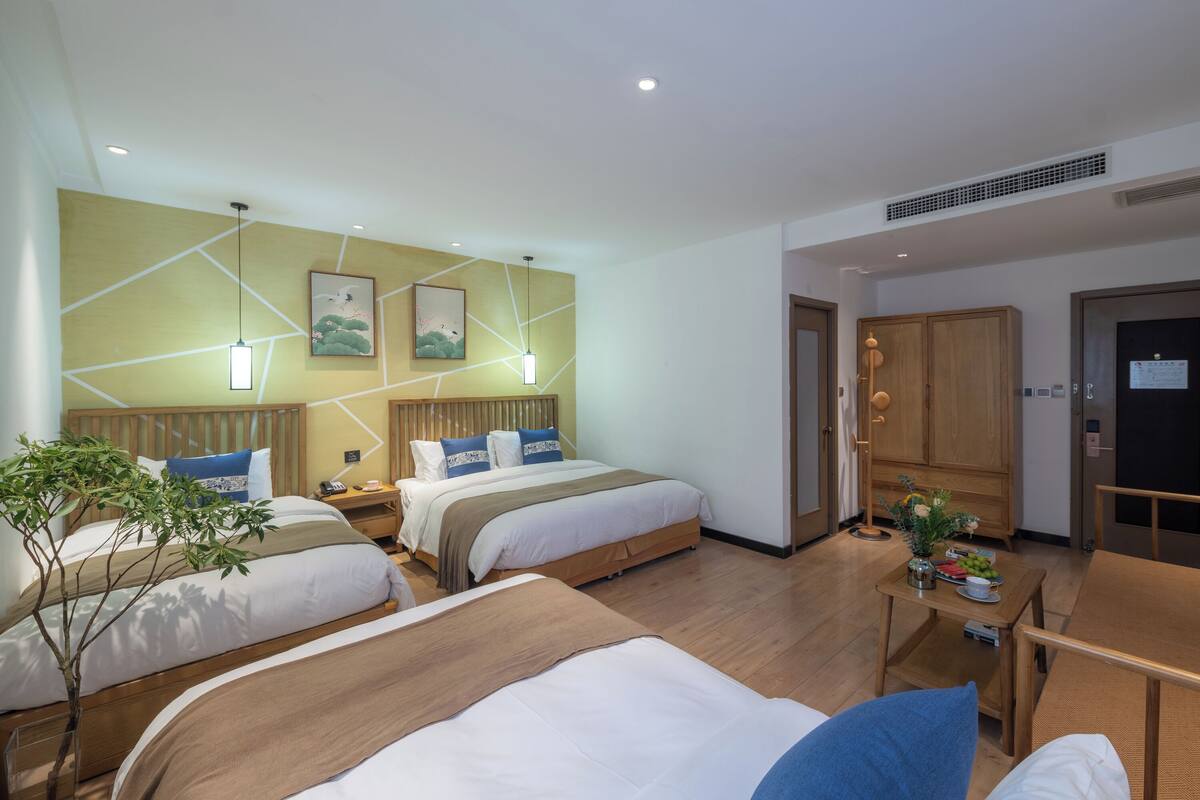 Une chambre d’hôtel avec deux lits, une tête de lit en bois, une petite table avec un vase et une porte avec une pancarte.