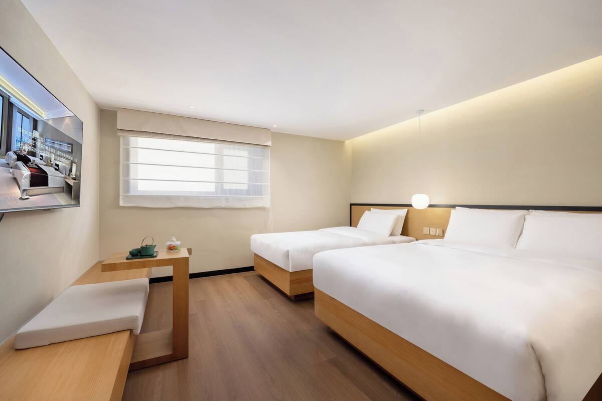 Une chambre d’hôtel avec deux lits, une petite table, une fenêtre et un téléviseur fixé au mur.