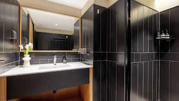 A modern bathroom with a large mirror, dark tiled walls, a white sink, and a shower area.
