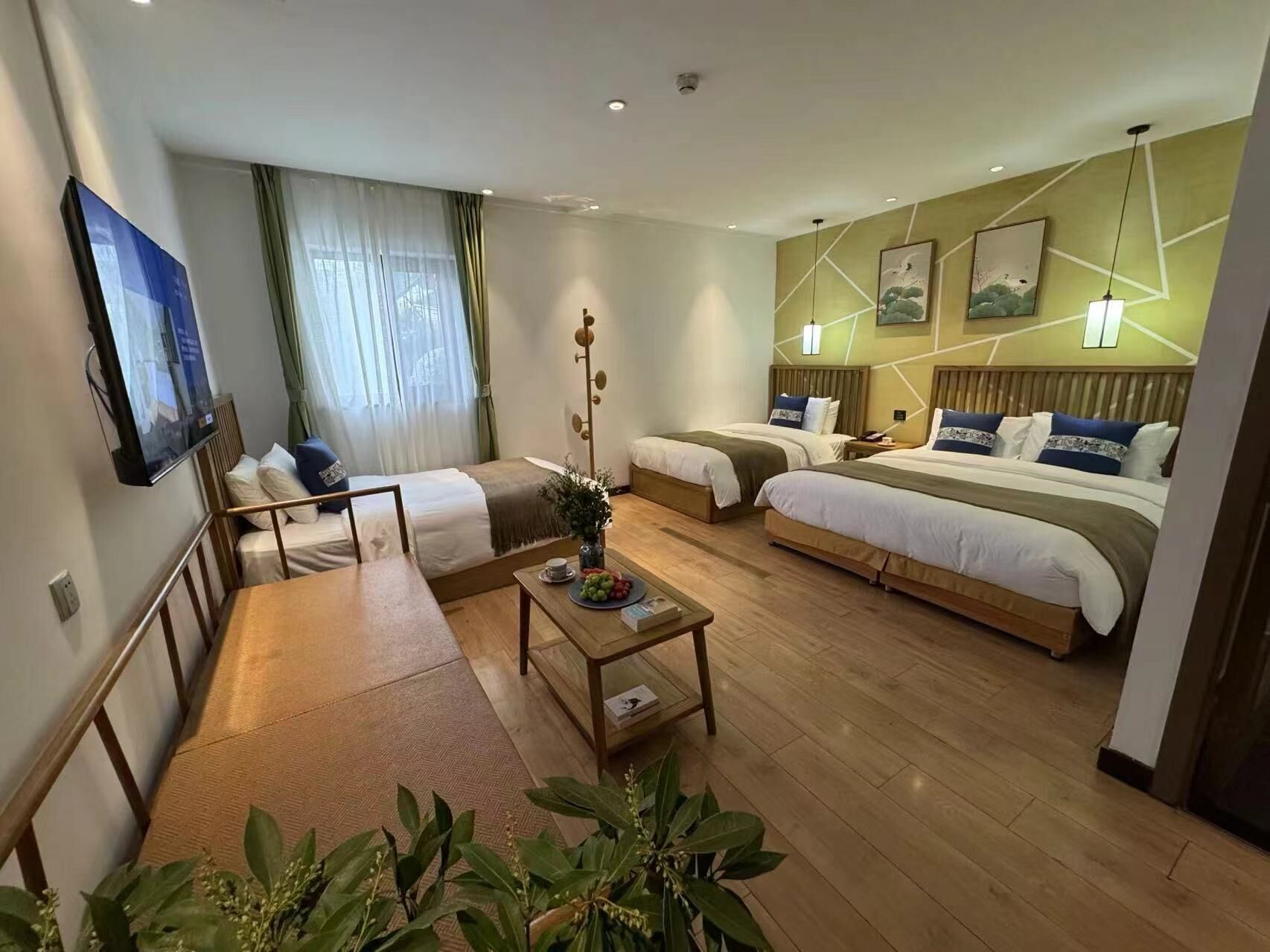 A hotel room with two beds, a dining table, a TV, and a large window with curtains.