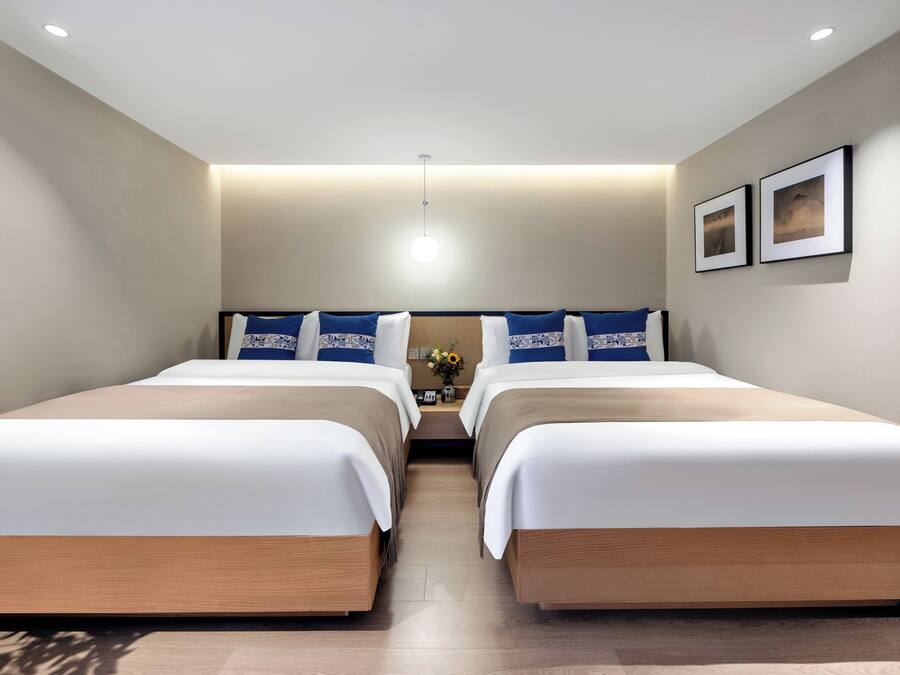 A hotel room with two beds, a nightstand with a vase of flowers, and two framed pictures on the wall.