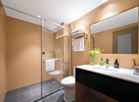 A modern bathroom with a glass shower enclosure, a white toilet, a black sink with a mirror above it, and a vase with flowers on the sink counter.