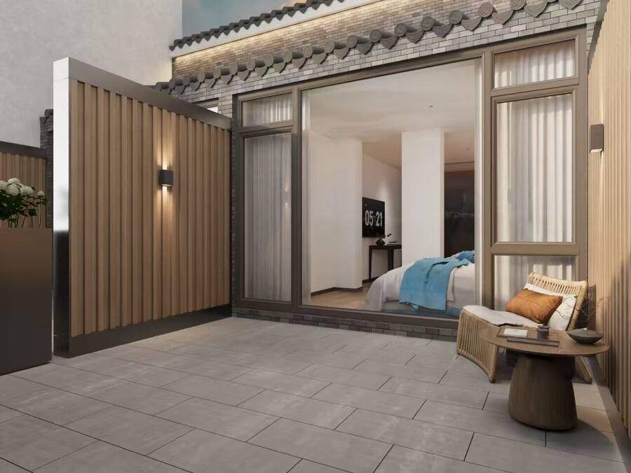 A modern hotel room with a sliding glass door leading to a balcony, a bed with a blue blanket, and a wicker chair with a cushion.
